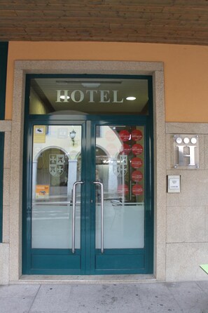 A hotel entrance with a glass door, a sign above the door, and a logo on the wall.