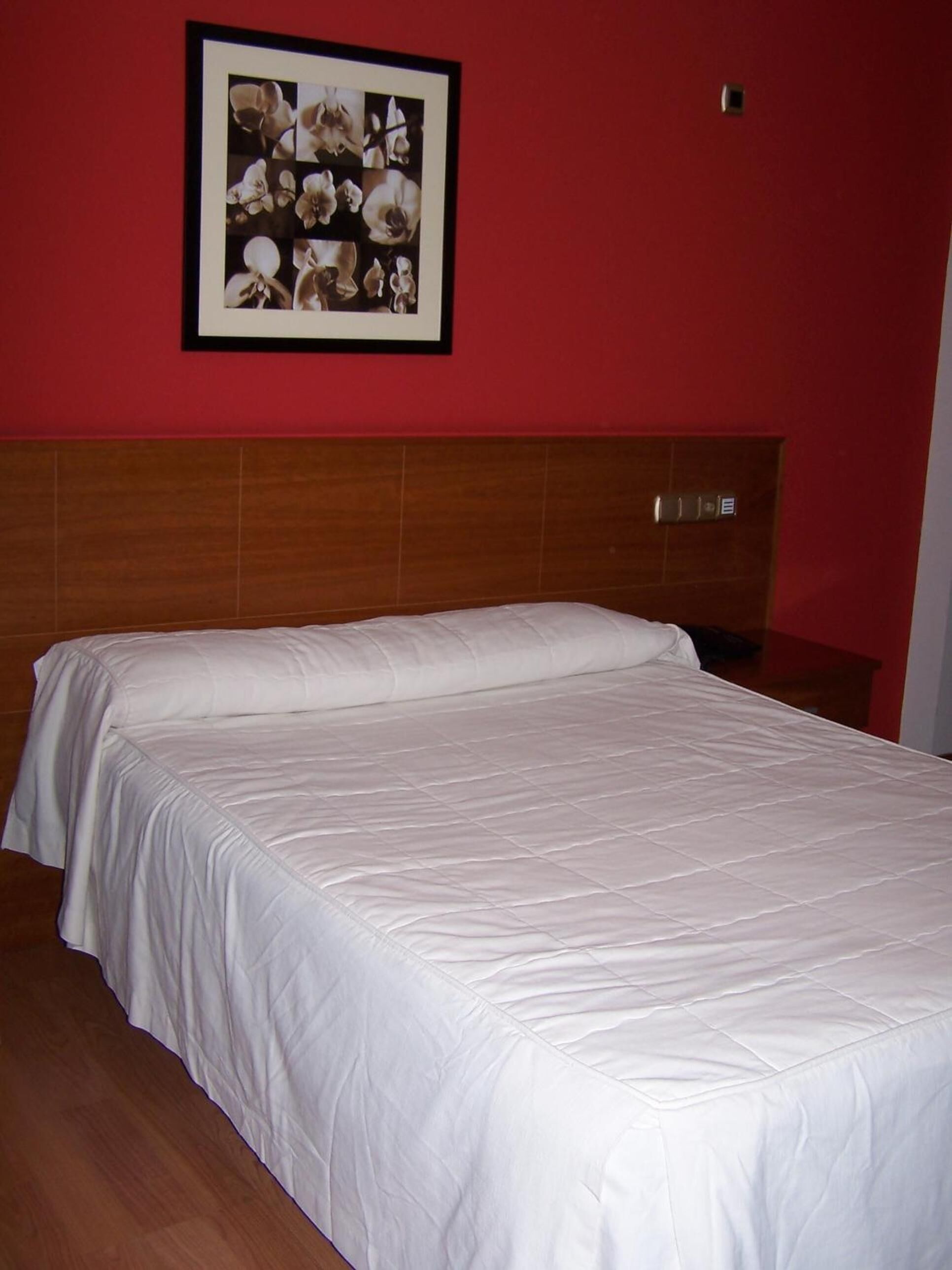Habitación de hotel con una cama grande, cabecero de madera, pared roja y un cuadro con flores.