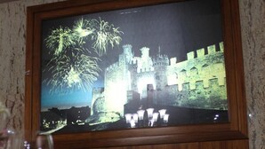 A dining table set with wine glasses, a plate, and cutlery, with a framed picture of fireworks and a castle on the wall behind. - El Castillo (Ponferrada)