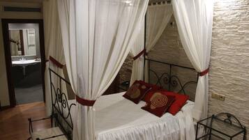 A bedroom with a four-poster bed, a chair, and a mirror.