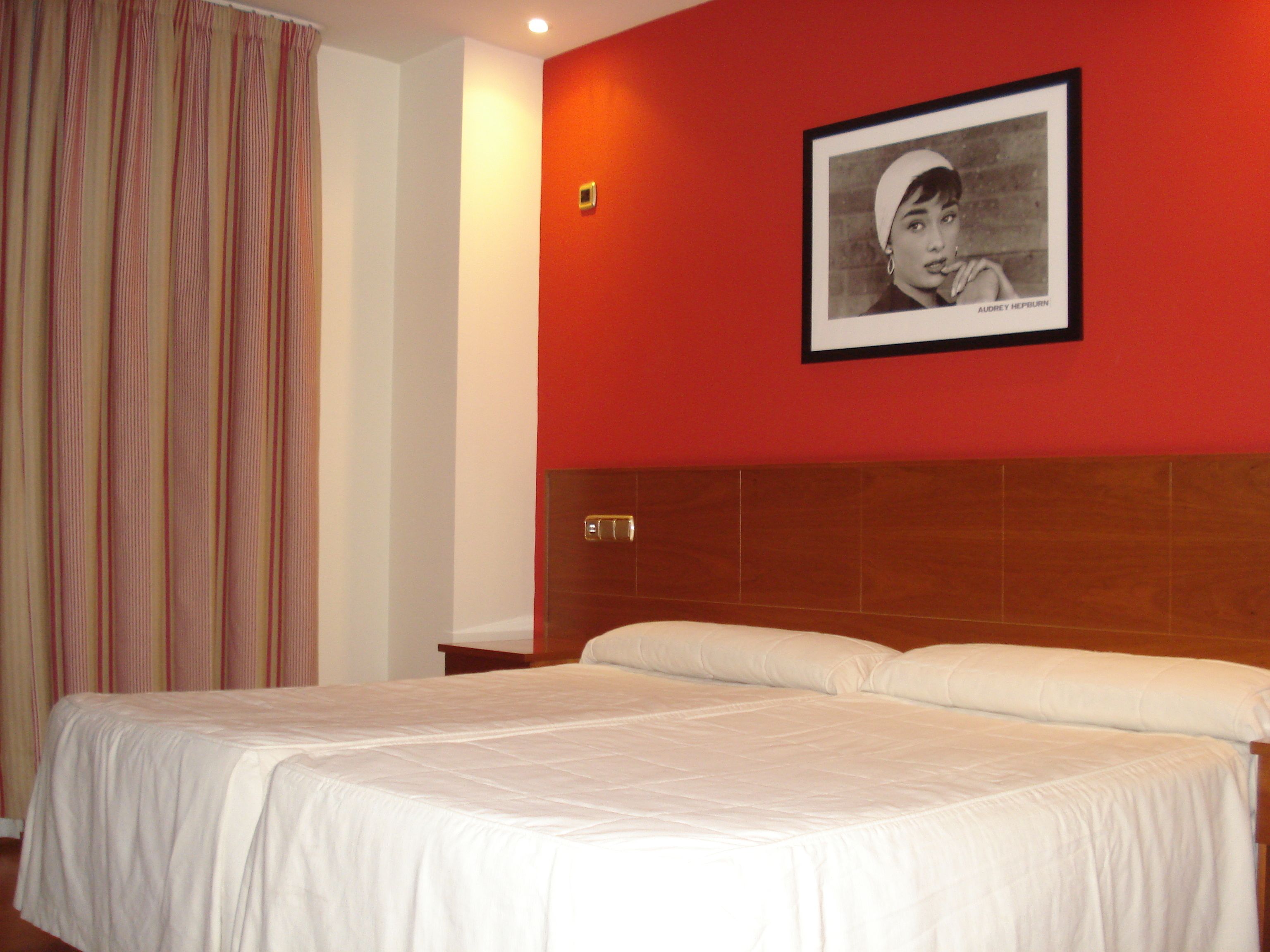 A hotel room with a bed, a framed picture on the wall, and a curtain.