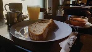 A table with a plate of bread, a glass of orange juice, a salt shaker, and a bowl of soup.
