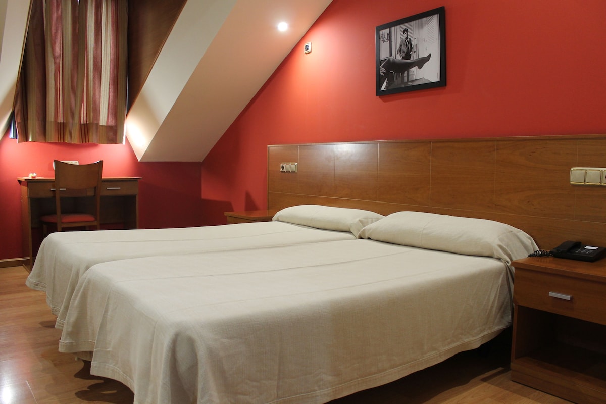 Habitación de hotel con dos camas, cabecera de madera, un escritorio y una silla.