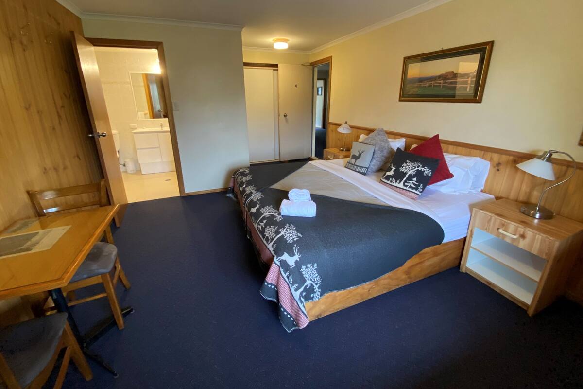 A bedroom with a bed, bedside table, chair, and a desk.