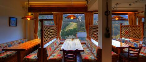 A dining area with wooden benches and tables, large windows with curtains, and hanging light fixtures.