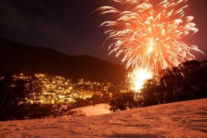 A nighttime view of a town with a large firework display. - Candlelight Lodge (Thredbo)