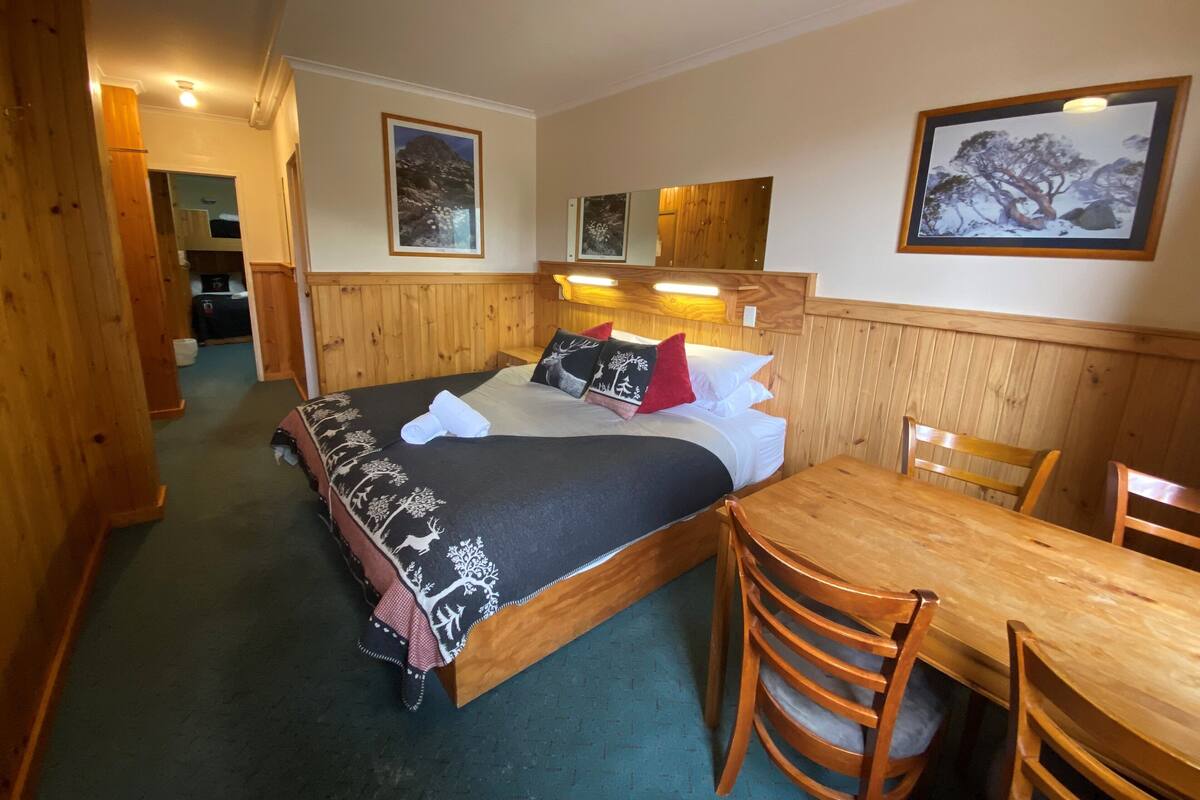 A wooden room with a bed, a table, and chairs. There are framed pictures on the walls.