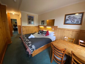 A wooden room with a bed, a table, and chairs. There are framed pictures on the walls. - Candlelight Lodge (Thredbo)