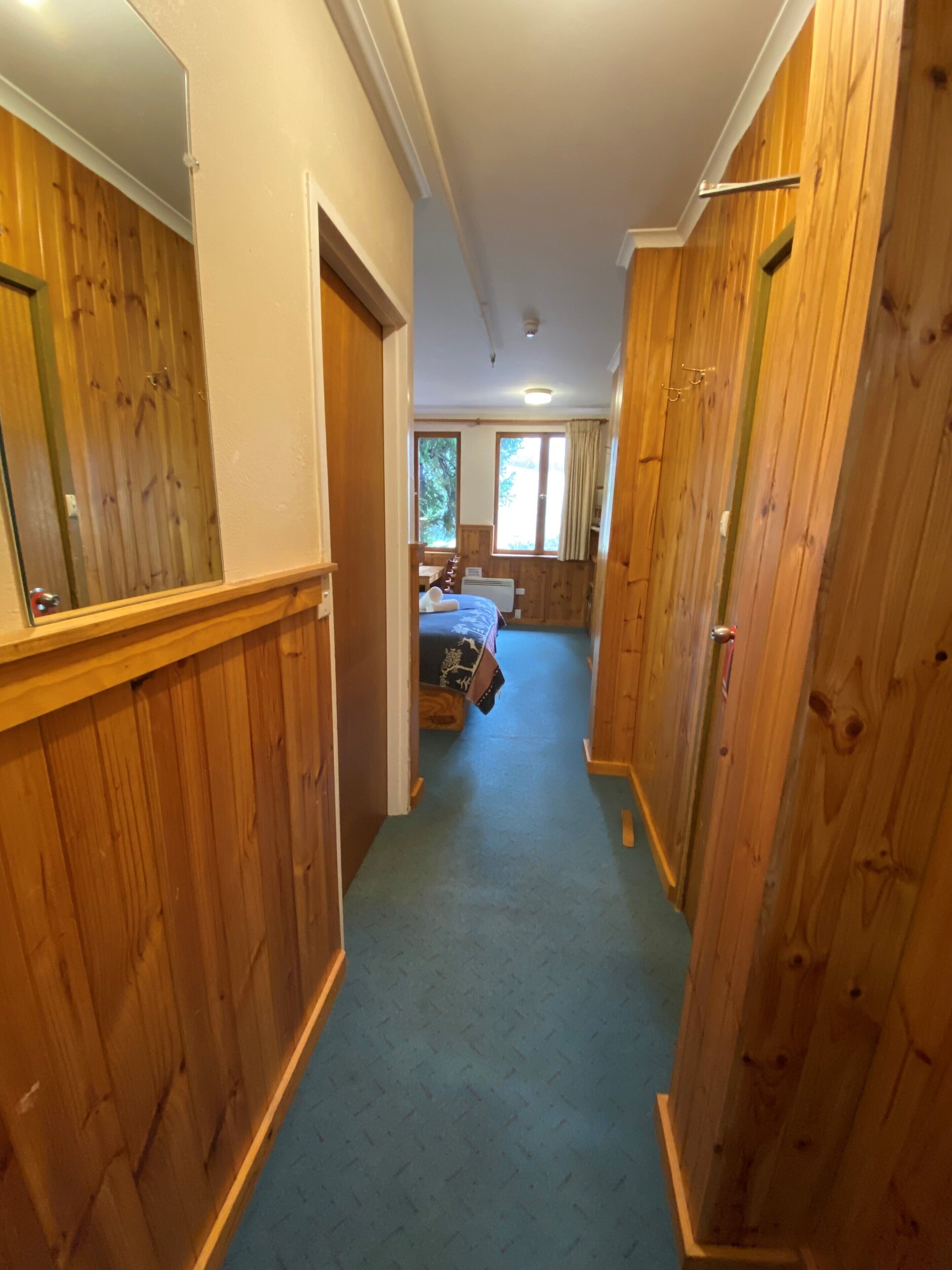 Un pasillo estrecho con paredes de madera y una alfombra azul que conduce a un dormitorio con cama y ventana.