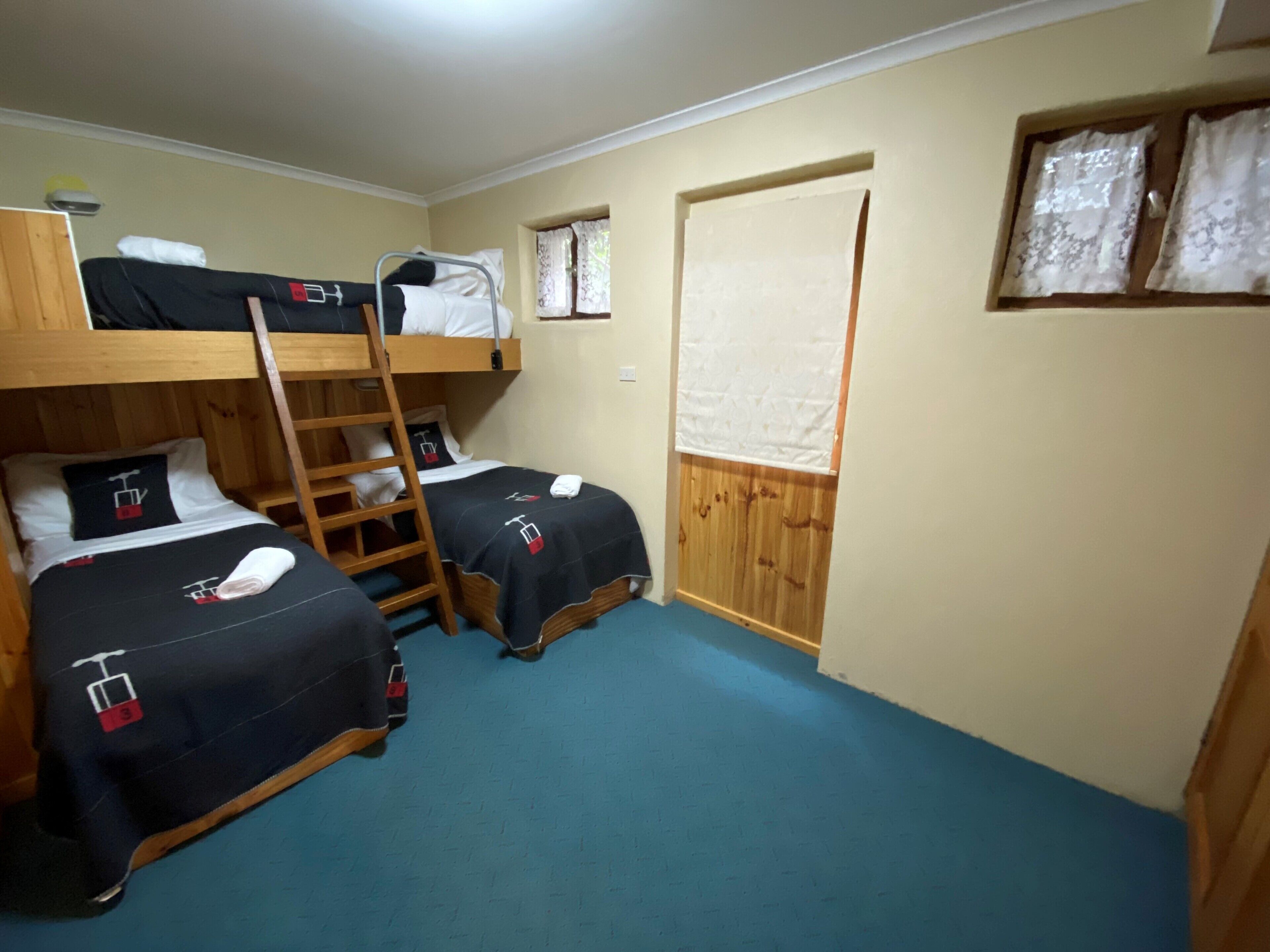 A room with bunk beds, a wooden ladder, and a window with curtains.
