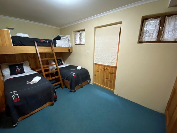 Una habitación con literas, una escalera de madera y una ventana con cortinas.