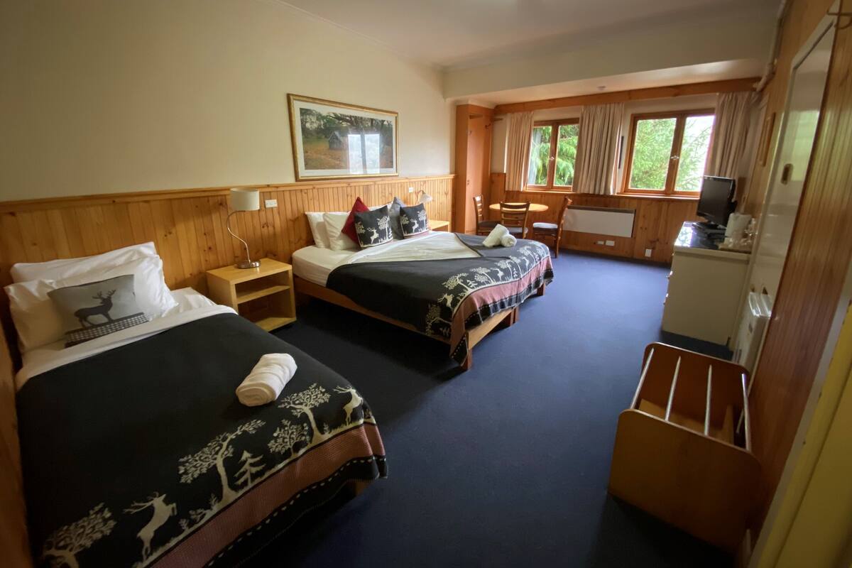 A hotel room with two beds, a desk, a chair, a television, and a window with curtains.