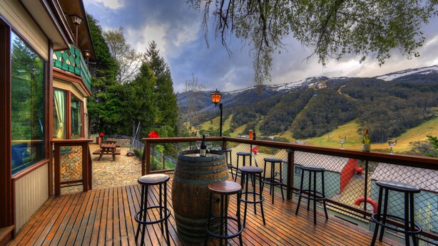A wooden deck with bar stools, a wooden barrel, and a view of a mountainous landscape.