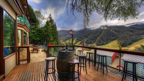 Una terraza de madera con taburetes de bar, un barril de madera y vistas a un paisaje montañoso.