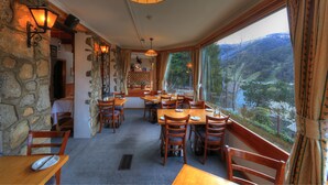 A dining area with stone walls, wooden tables, and chairs, overlooking a scenic valley.