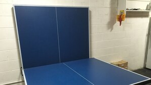 A blue ping pong table in a room with white brick walls and a tiled floor.