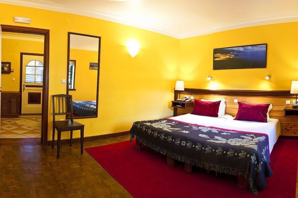 A hotel room with a bed, a chair, a red rug, and a wooden floor.