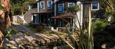 Une maison en pierre avec un jardin, un étang et un sentier.