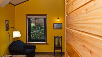 A room with a yellow wall, a window with a view of trees, a lamp, a chair, and a wooden panel wall.
