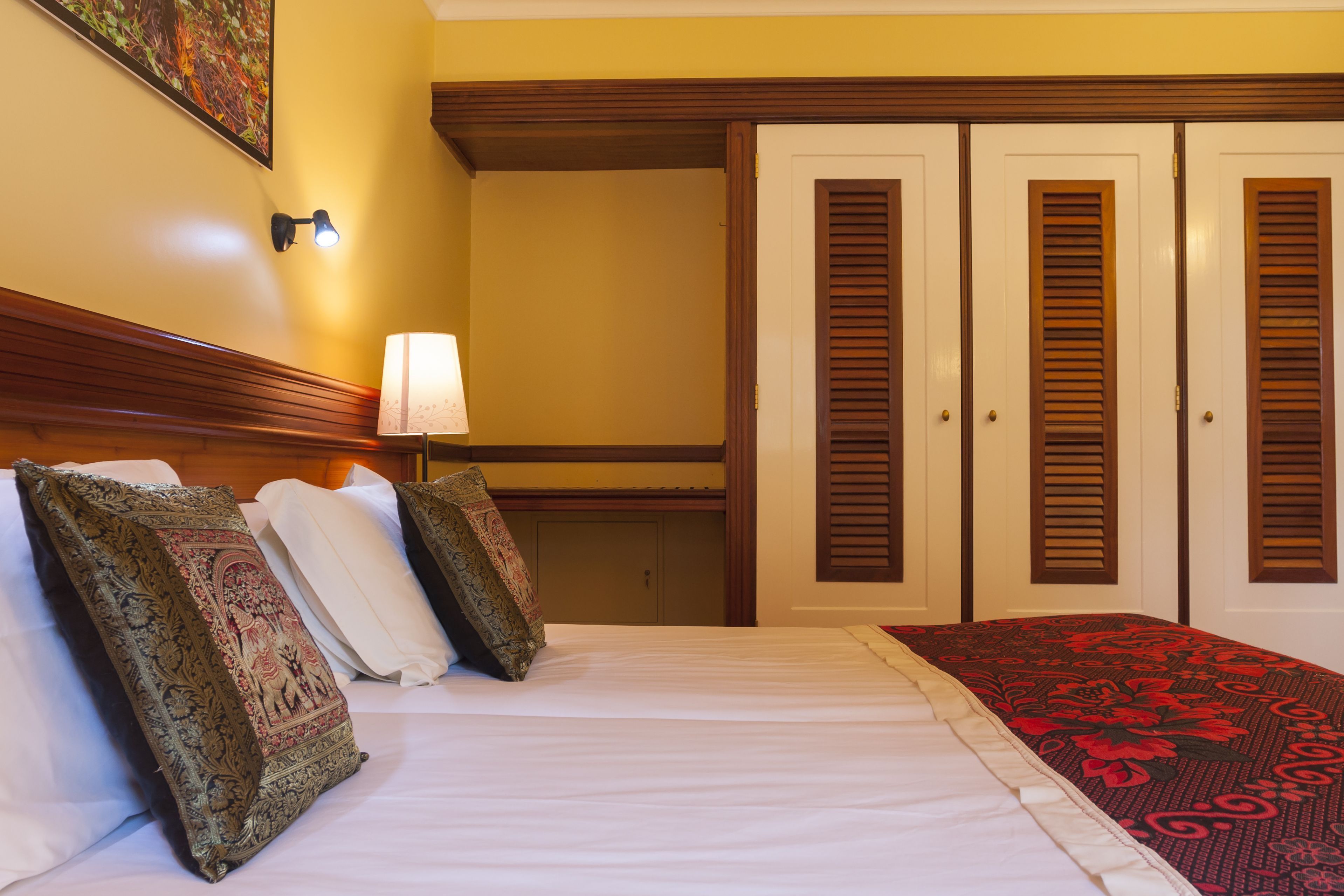 Ein Hotelzimmer mit Bett, Kissen, Lampe und Kleiderschrank.
