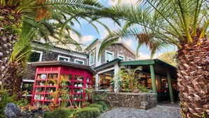 A tropical resort with a cobblestone courtyard, palm trees, and a red building with a green roof.