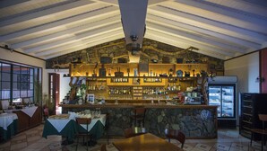 A restaurant with a high ceiling, stone walls, a bar area with shelves of bottles, and a tiled floor.