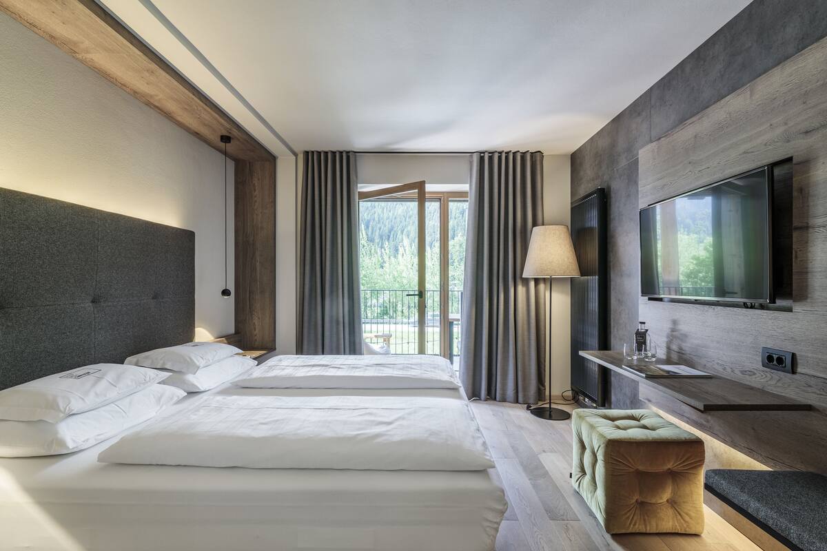 A modern hotel room with a large bed, a TV mounted on the wall, and a balcony with curtains.