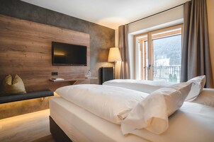 Habitación de hotel con una cama grande, un televisor de pantalla plana montado en una pared de madera, una mesita de noche con lámpara y una ventana con cortinas.