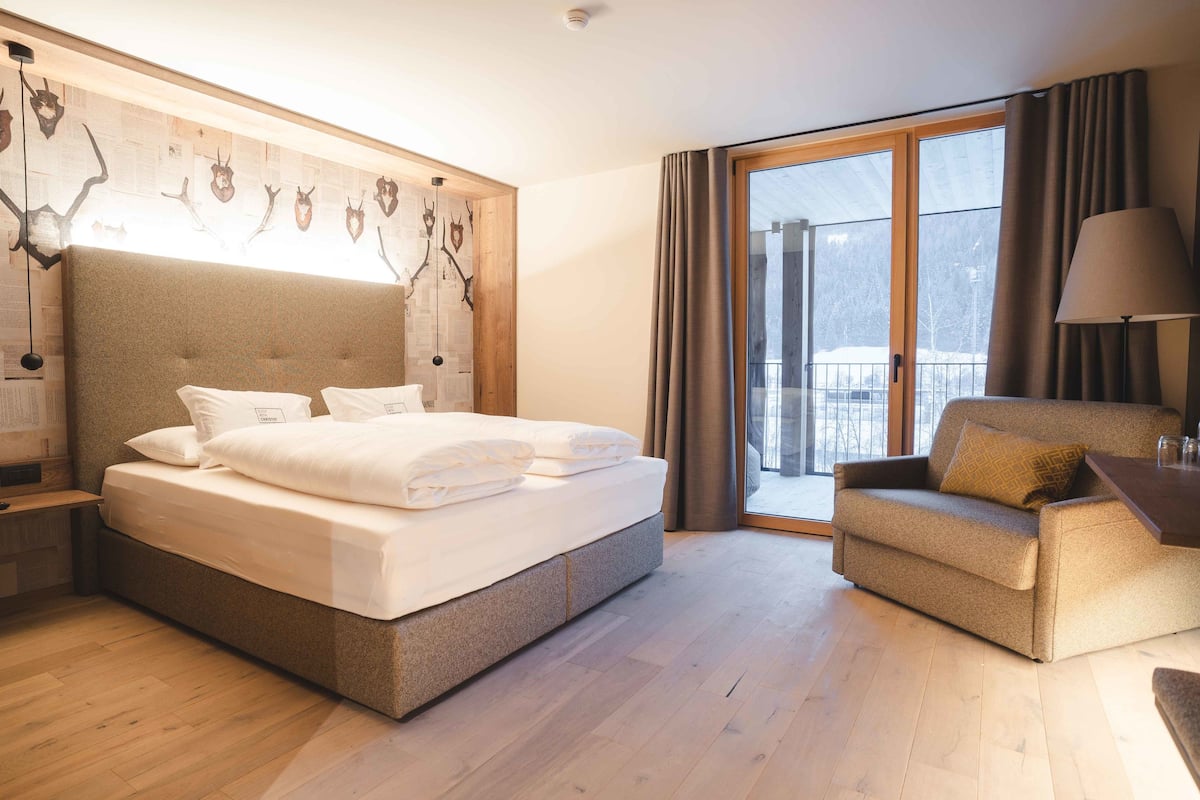 A hotel room with a large bed, a sofa, a desk, and a view of the outdoors.