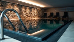 A modern indoor swimming pool with a stone wall backdrop, seating area, and a motivational sign. - Christof Hotel (Monguelfo)