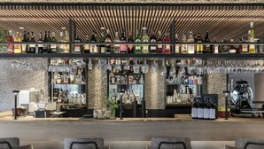 A bar area with multiple shelves of bottles and glasses, a coffee machine, and seating with chairs. - Christof Hotel (Monguelfo)