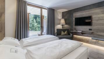 A hotel room with two beds, a TV mounted on a wooden wall, a chair, and a balcony with curtains.