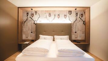 A double bed with white linens, a wooden headboard, and a wall-mounted display of animal horns.