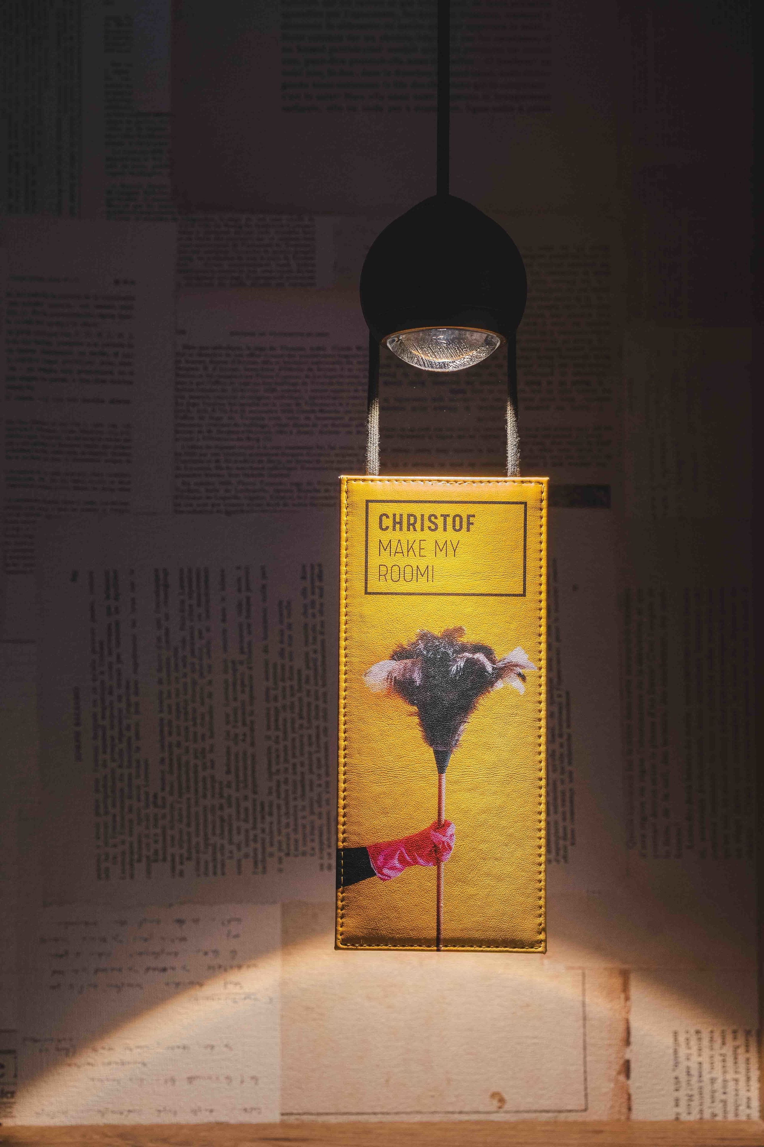 A book titled "Christof Make My Room" hanging from a black ceiling fixture.