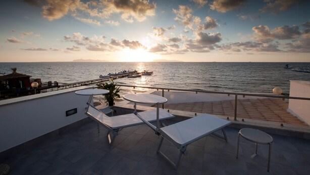 A terrace with white lounge chairs and tables overlooking the sea at sunset. - Sunset Beach (Misiliscemi)