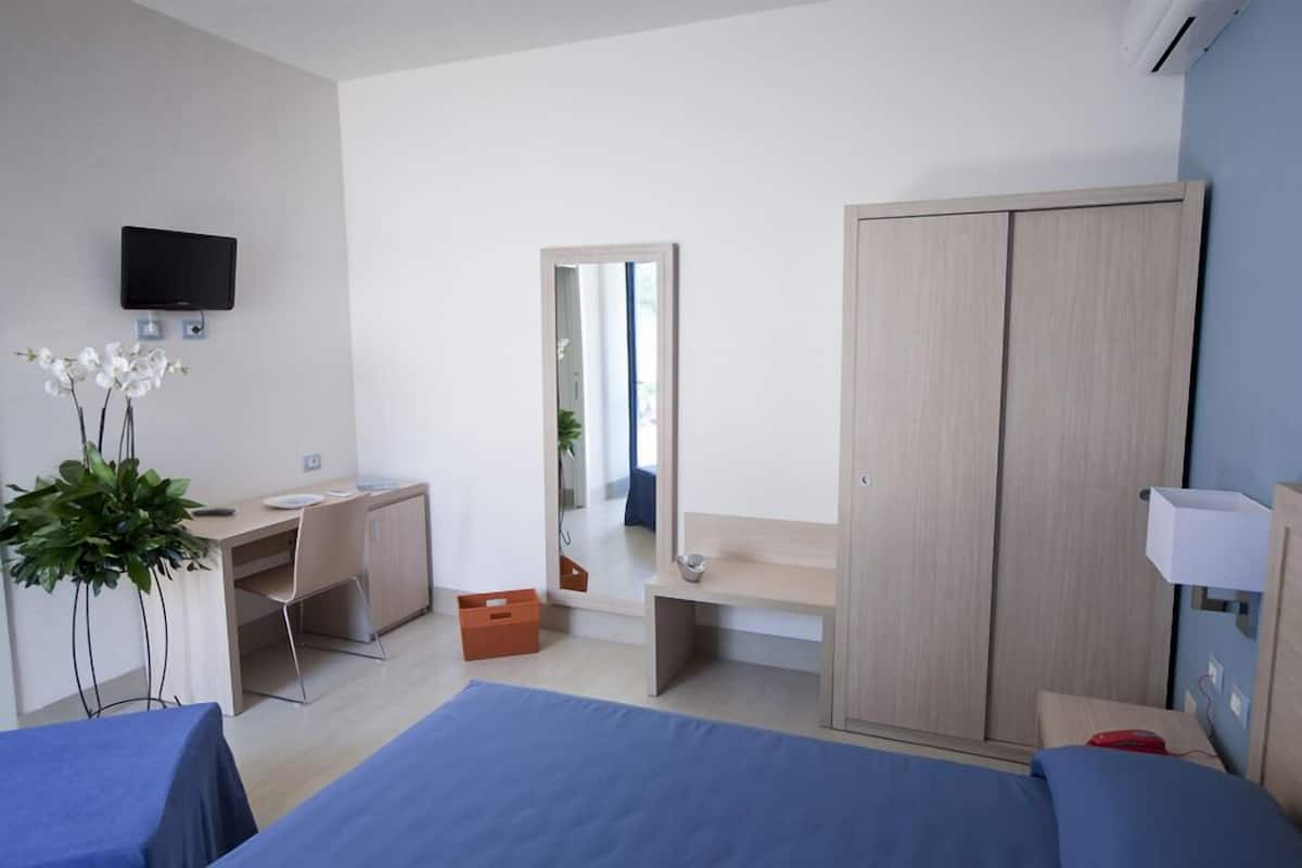 A hotel room with a bed, a desk, a wardrobe, a TV, and a mirror.