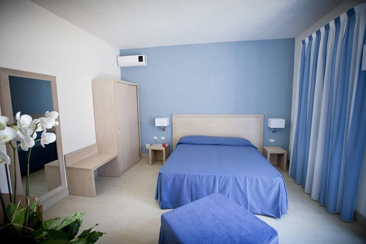 A hotel room with a large bed, bedside tables, a wardrobe, and a mirror.
