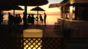 A beachside restaurant with outdoor seating, umbrellas, and a view of the sunset over the water. - Sunset Beach (Misiliscemi)
