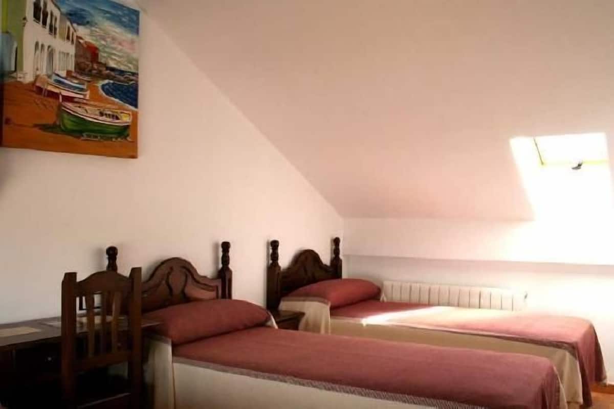 A bedroom with two single beds, a wooden chair, a painting, and a window with a view of the sea.