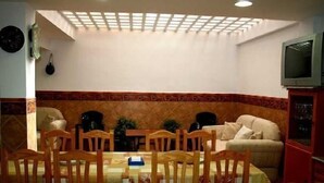 A dining area with a round table, wooden chairs, a sofa, and a television on a cabinet.