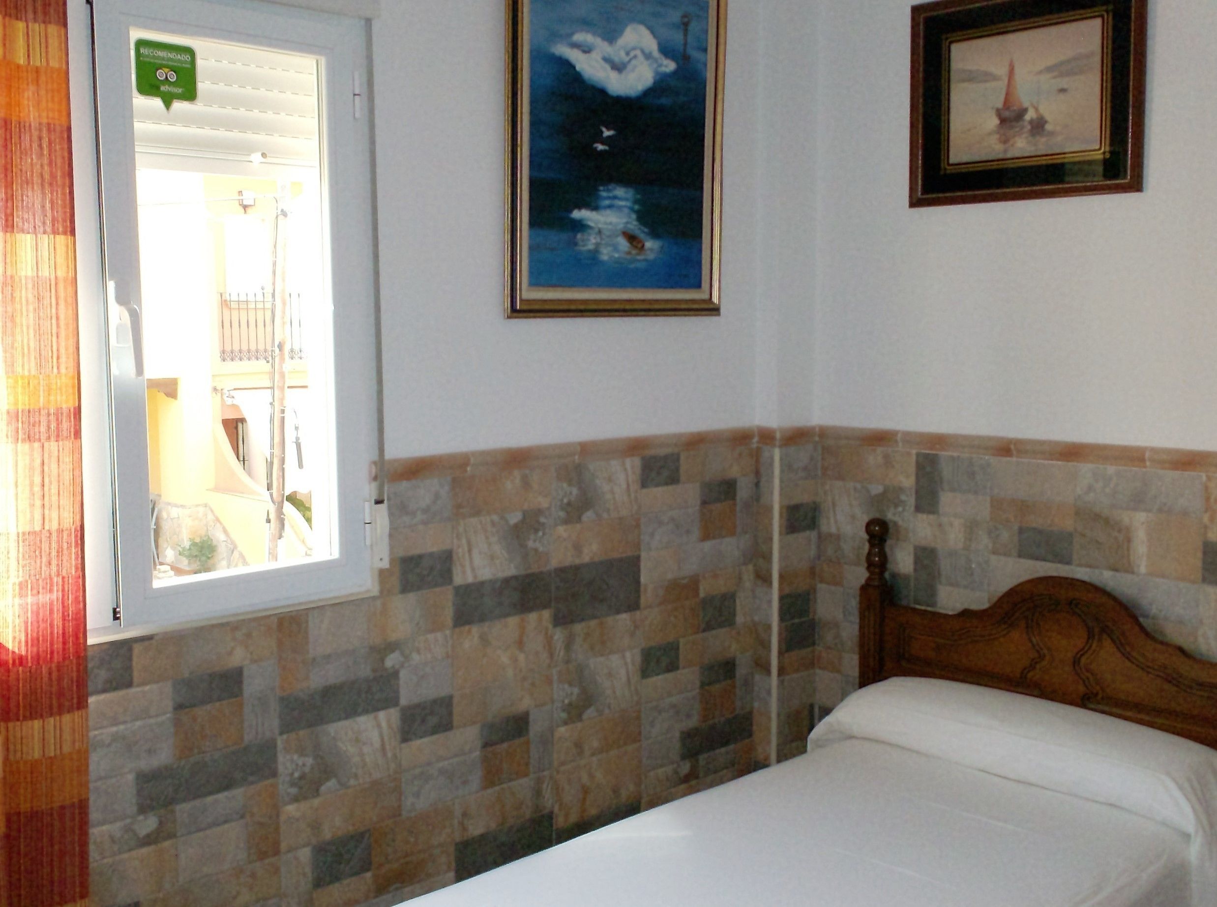 Un dormitorio con cama, ventana con persianas, pared con azulejos y un cuadro enmarcado.