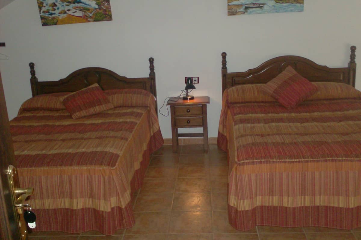 Two single beds with wooden headboards, a nightstand with a lamp, and two paintings on the wall.