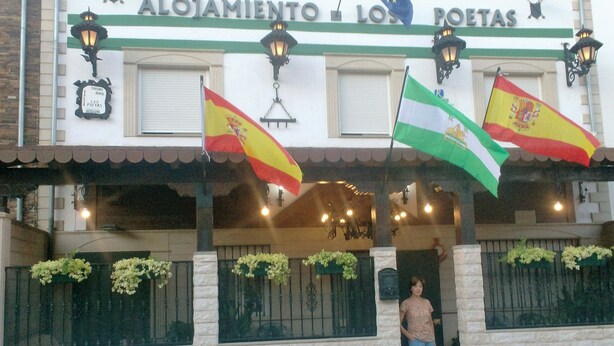 A building with the sign "Alojamiento Los Poetas" and multiple flags, including the Spanish flag.