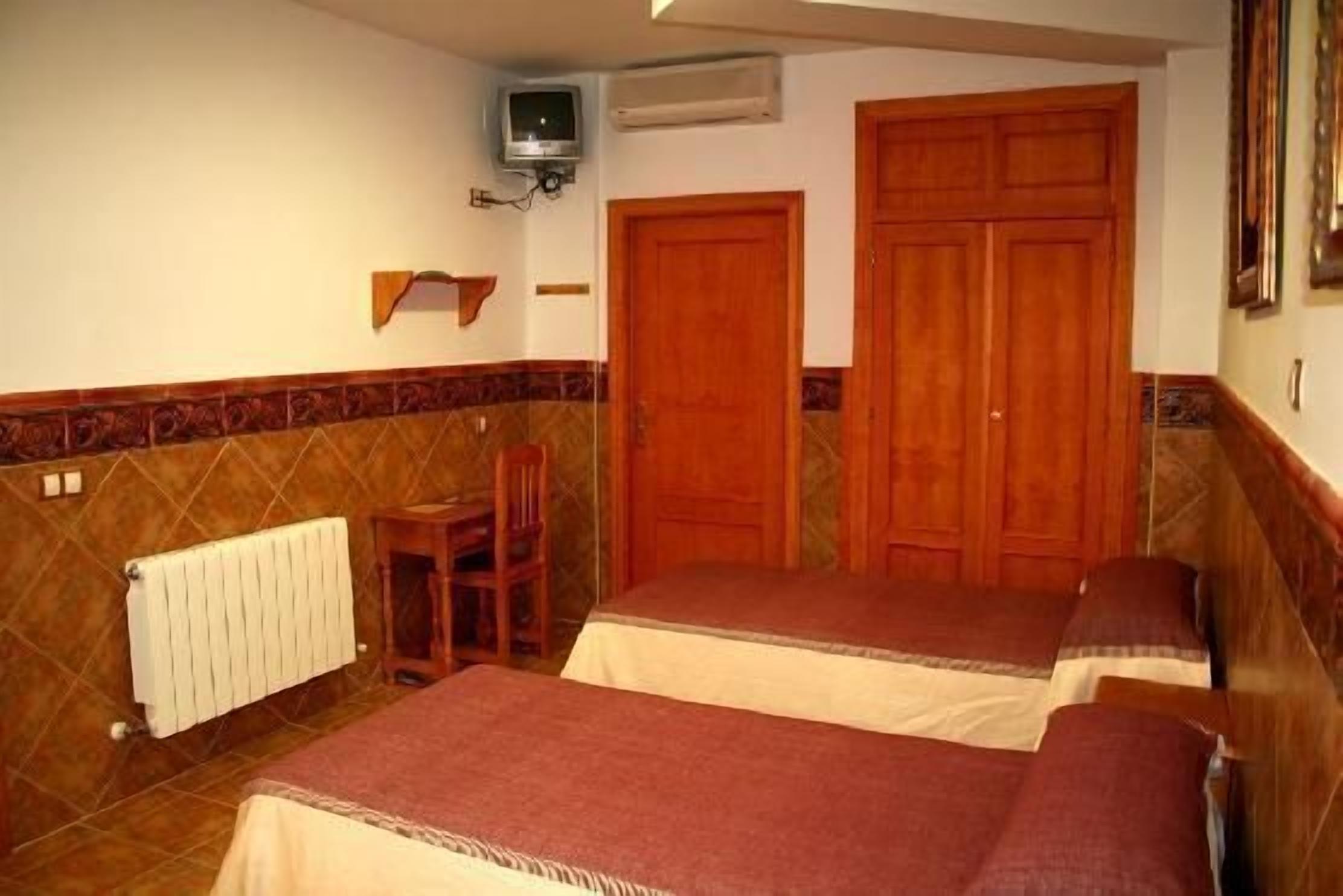 A room with two beds, a chair, a radiator, and a television.