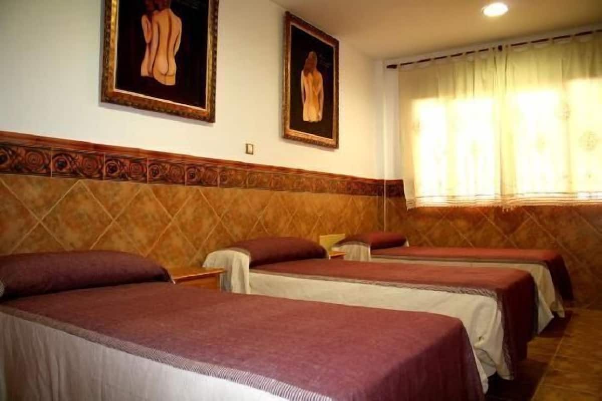 A hotel room with three beds, each with a red blanket, and two framed artworks on the wall.