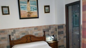 A neatly made bed with a white sheet and a wooden headboard, a bedside table with a lamp, and a painting of a beach scene on the wall.
