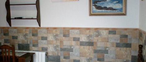 A room with a bed, a chair, a table, and a tiled wall.