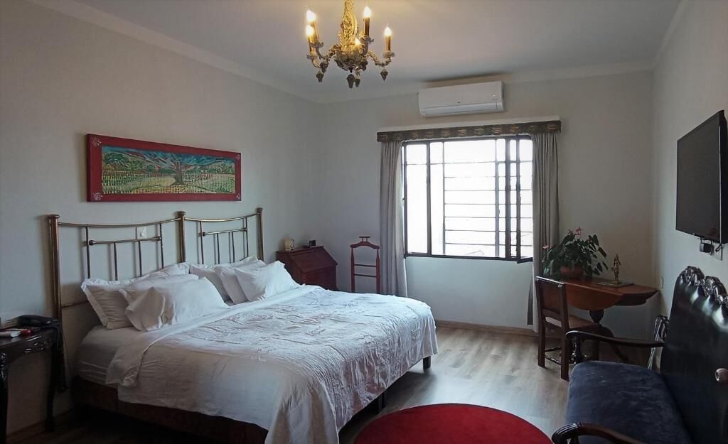 Un dormitorio con cama, escritorio, silla, televisor, ventana con cortinas y candelabro.