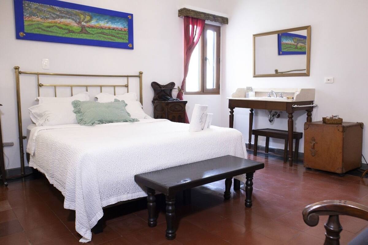A bedroom with a bed, a bench, a dresser, a mirror, and a window with curtains.