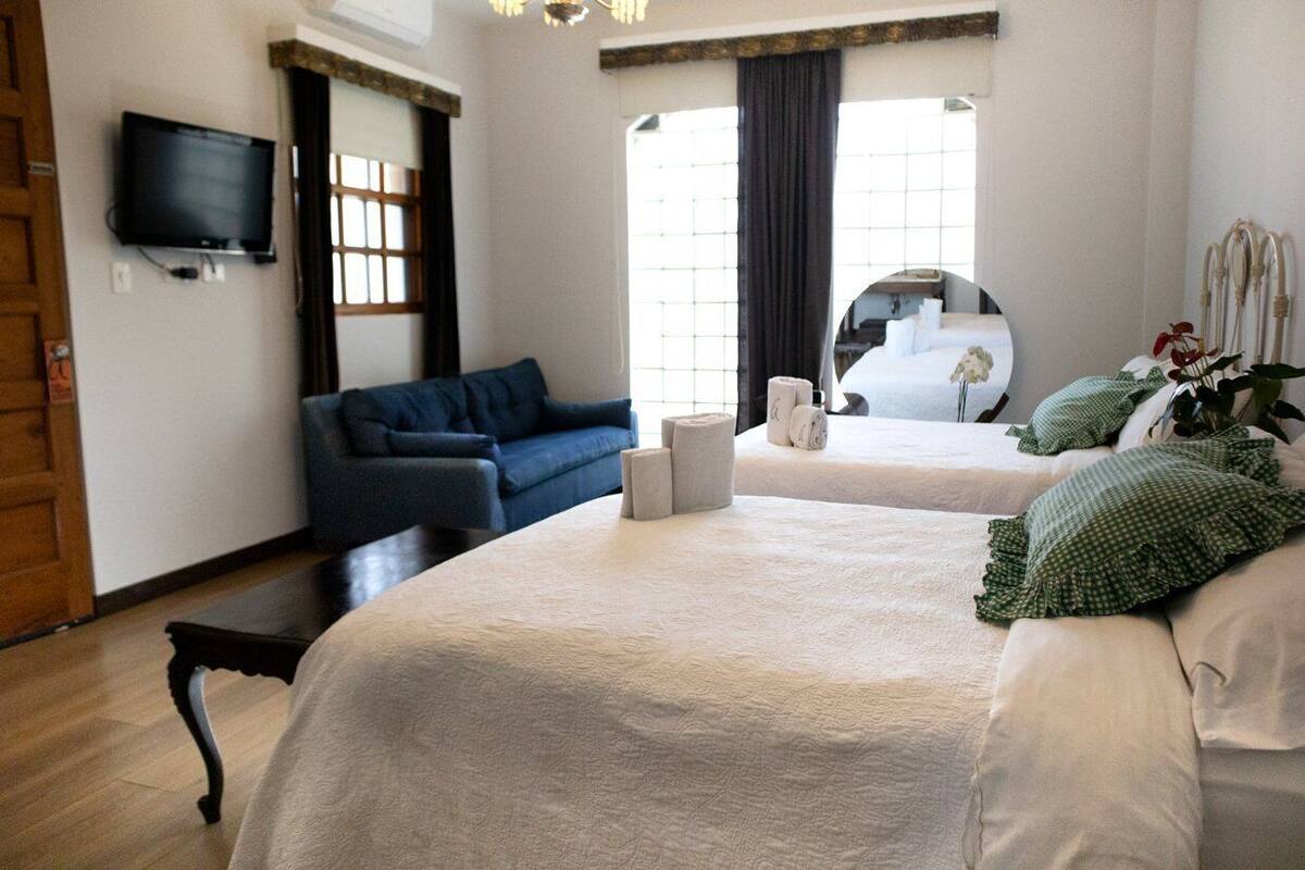 A hotel room with a large bed, a sofa, a TV, and a window with curtains.